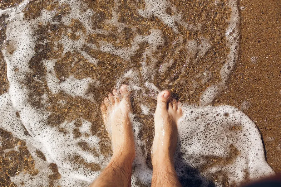 Bare feet standing in wet sand at the water's edge